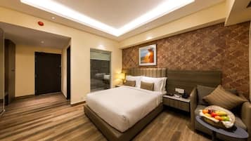A hotel room with a large bed, a bedside table with a lamp, a small sofa, and a fruit basket.
