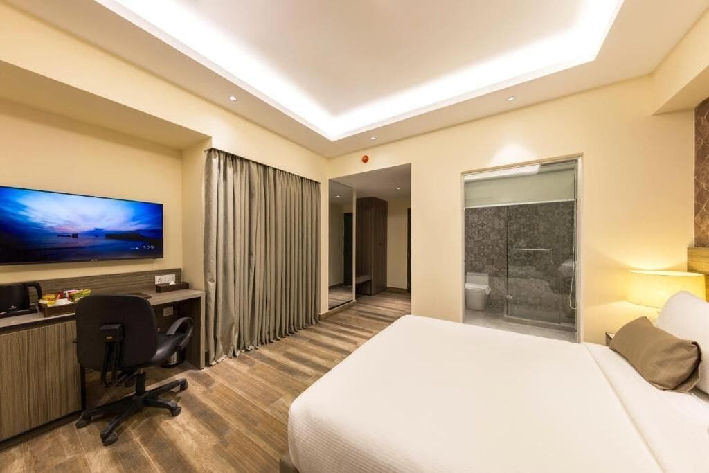 A hotel room with a bed, desk, chair, television, and a shower area.