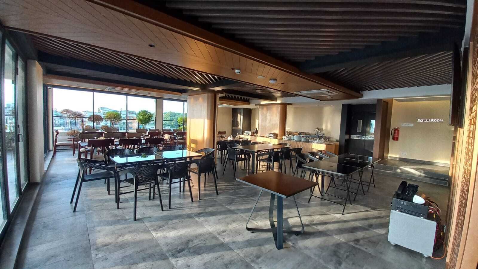 A modern dining area with tables and chairs, a kitchen area, and a view through large windows.