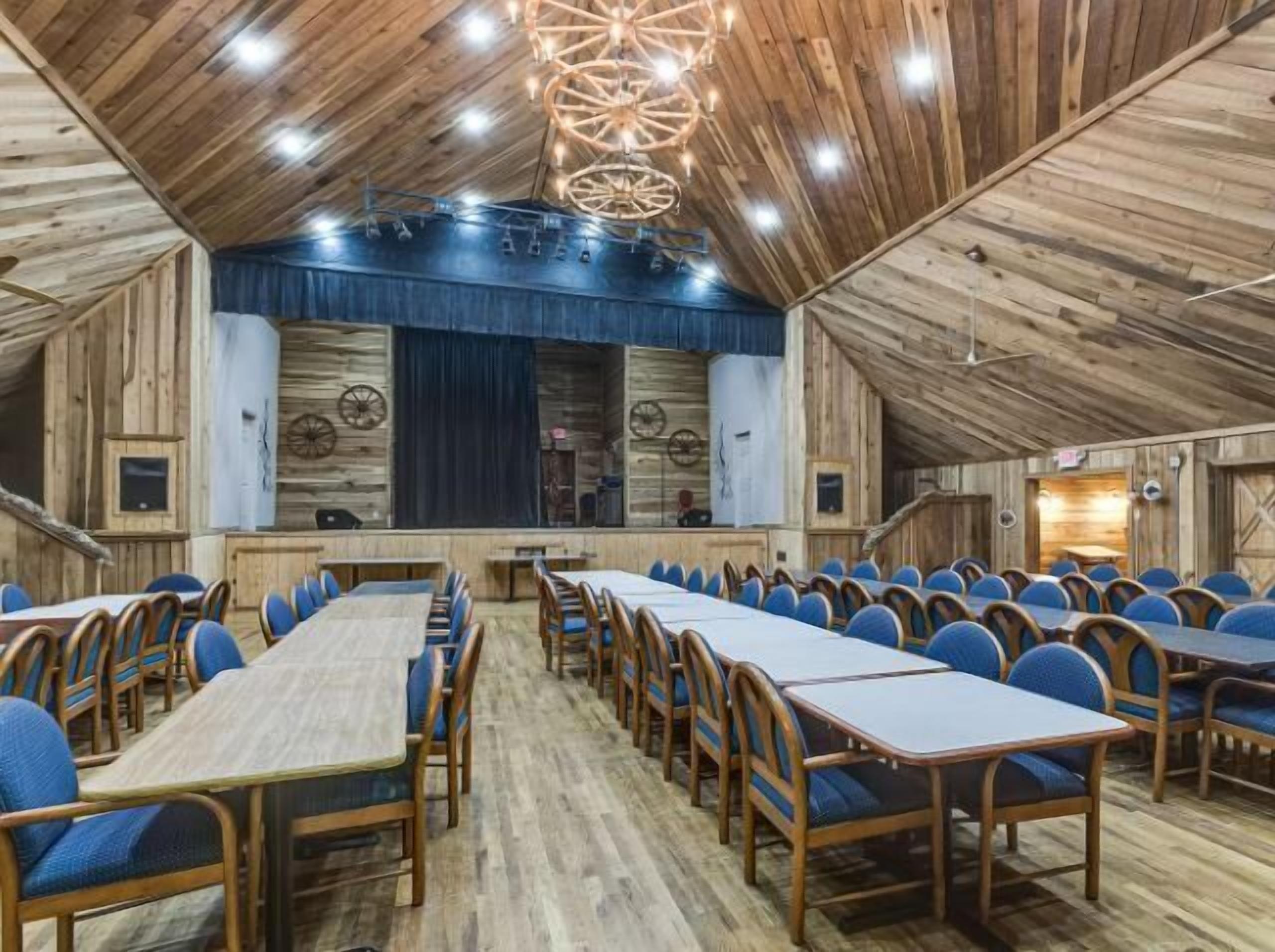 Une salle de conférence dotée de plusieurs tables et chaises, de murs en bois et d’un plafond avec des poutres apparentes et des luminaires.