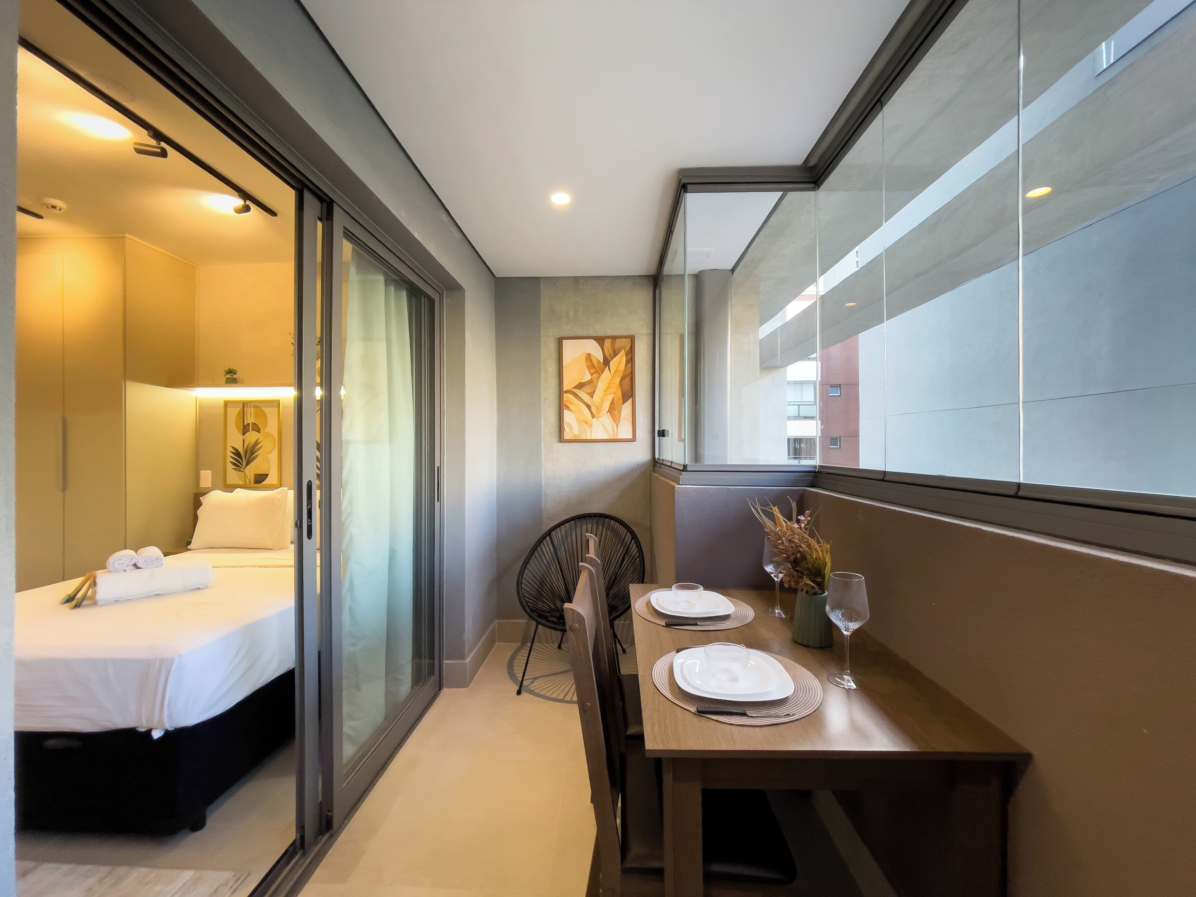 Habitació d'hotel amb un llit, una taula de dinar preparada per a dues persones i una vista per una porta de vidre.