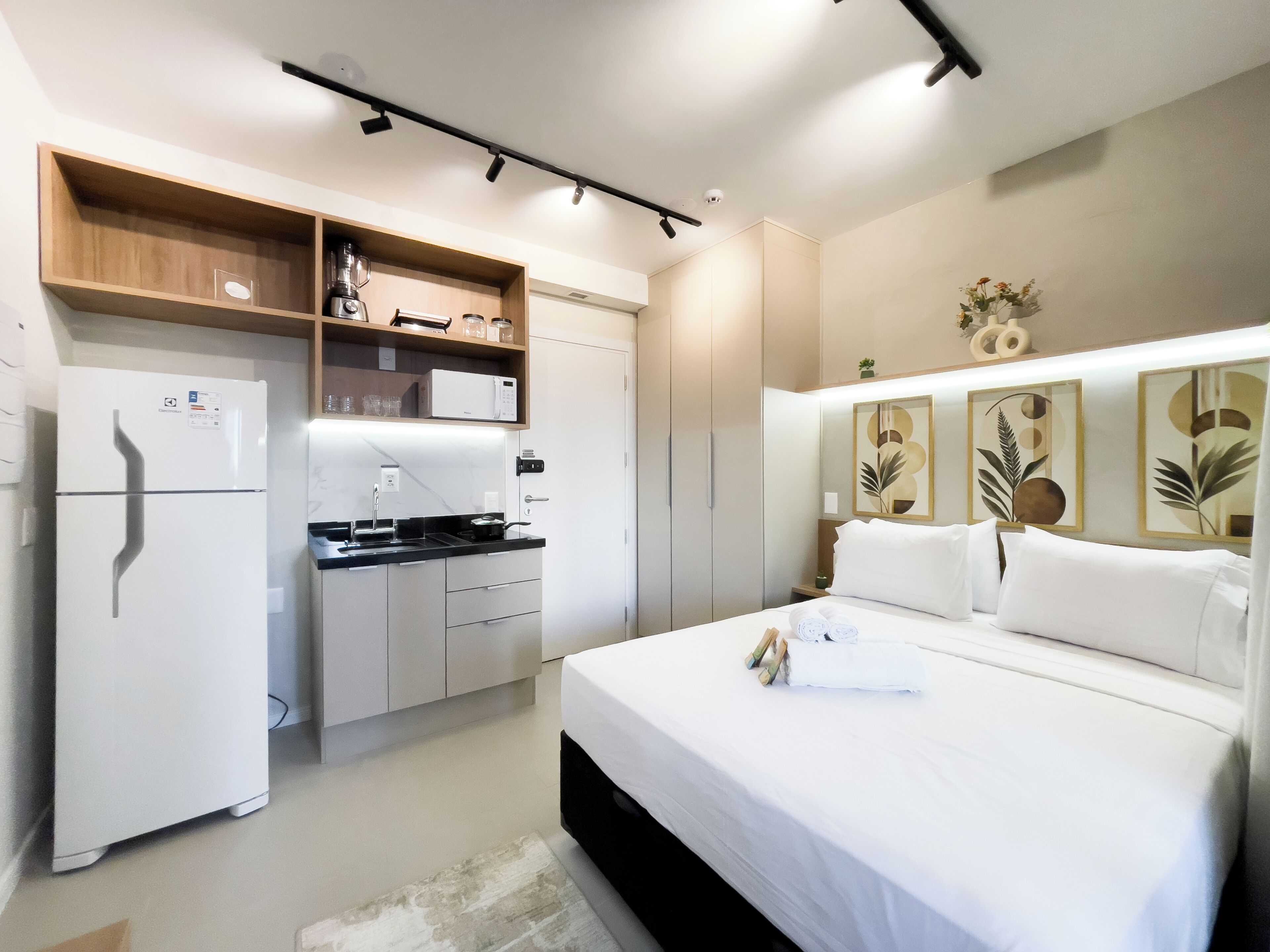 A modern hotel room with a bed, a kitchenette, and a bathroom.