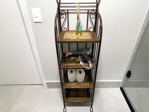 Uma estante de metal com um secador e garrafas na prateleira superior, e duas garrafas brancas na prateleira inferior.