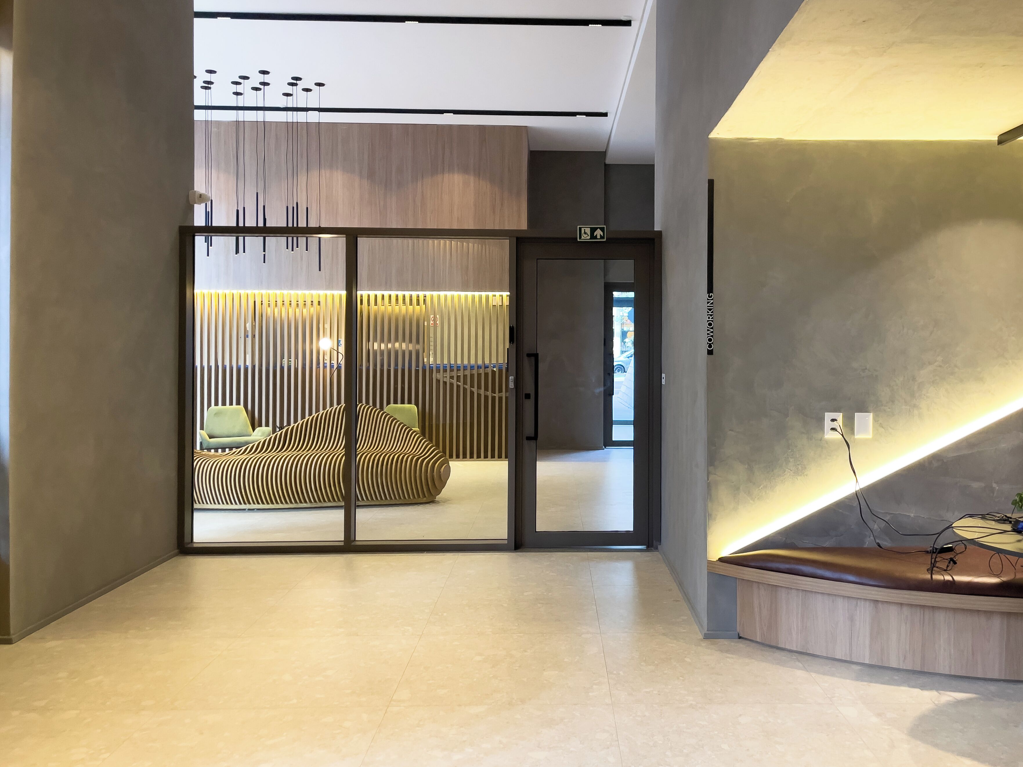Interior moderno com uma mesa de recepção, área de estar com um sofá estampado e uma porta de vidro que dá para outro espaço.
