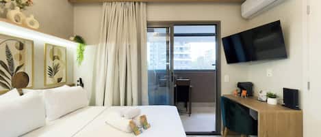 A modern hotel room with a bed, a desk, a television, and a view of the city through the window.
