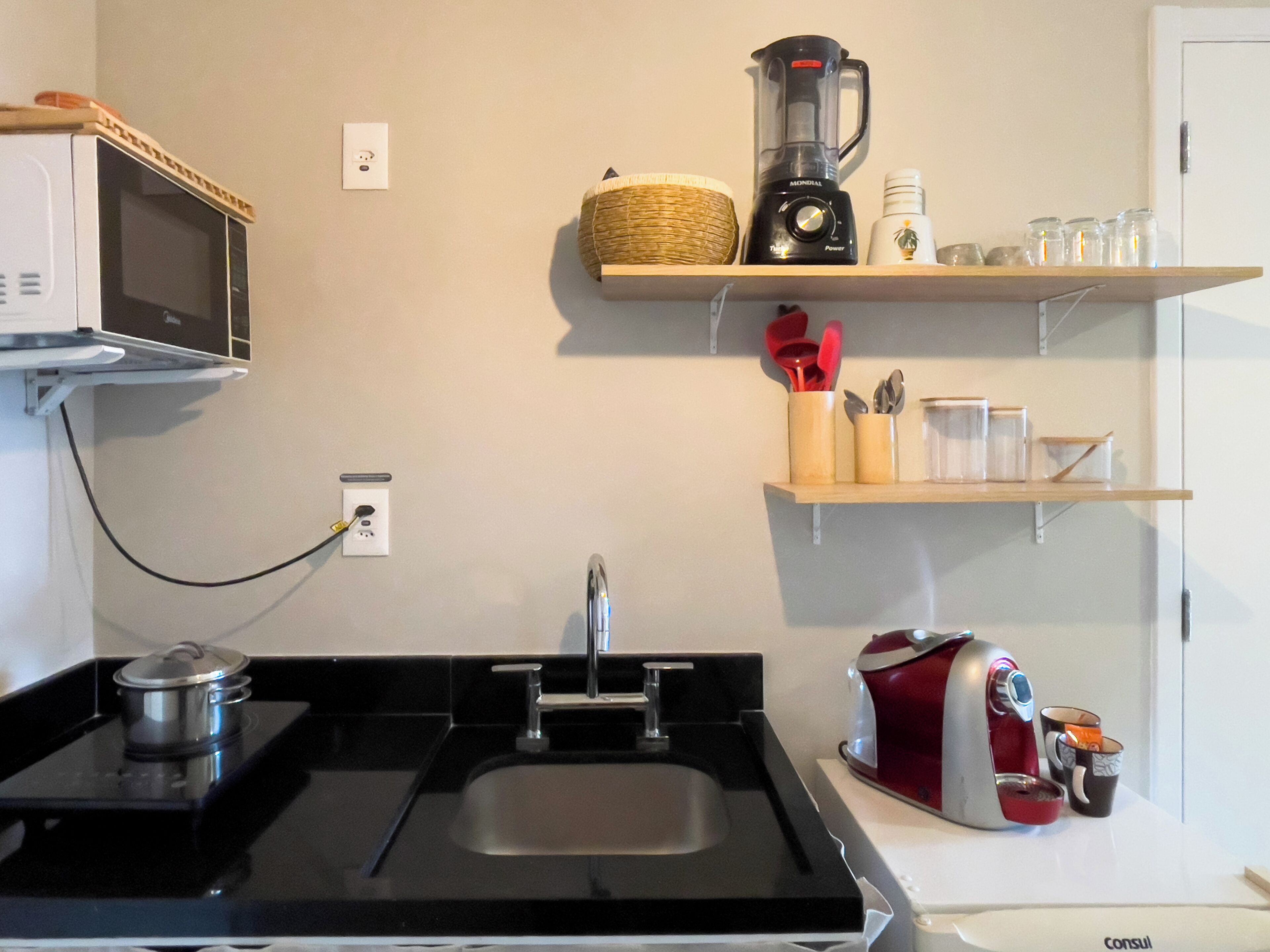 Eine Küche mit Mikrowelle, Mixer, Kaffeemaschine und verschiedenen Küchenutensilien in Regalen.