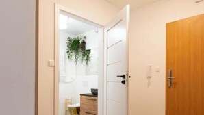 Un pasillo con piso de madera, un banco rojo, una puerta blanca y una puerta de madera.