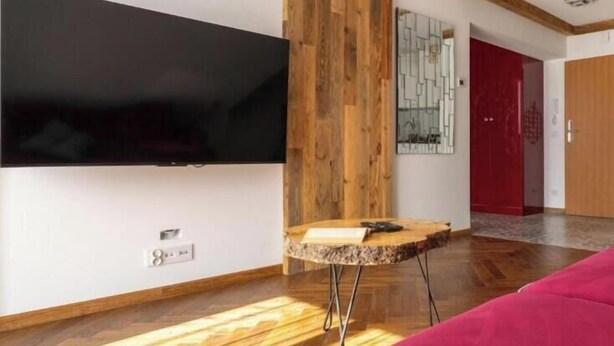 Una sala de estar moderna con un televisor de pantalla plana montado en la pared, piso de madera, una mesita redonda y un sofá rojo.