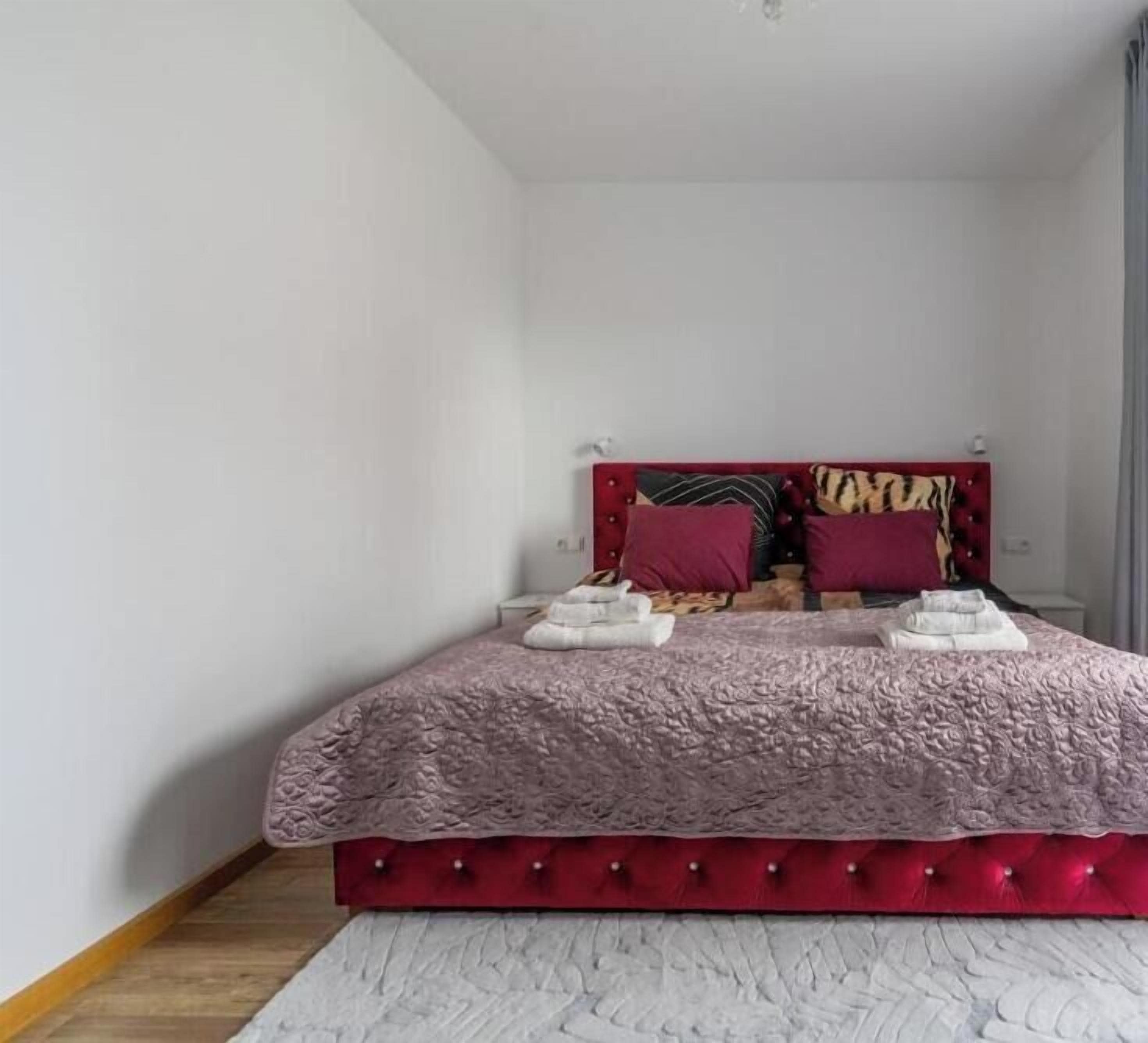 Ein Schlafzimmer mit einem roten, gepolsterten Kopfteil, einem weißen Teppich mit Struktur und einem Bett mit einer rosa Tagesdecke.