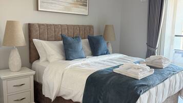 A bedroom with a large bed, bedside tables, a hanging light fixture, and a window with curtains.