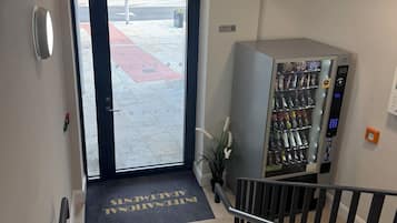 Ein Hotel Eingang mit Glastür, einem Rauchverbot-Schild, einem Verkaufsautomaten und einer Fußmatte mit der Aufschrift 'INTERNATIONAL AIRPORT'.