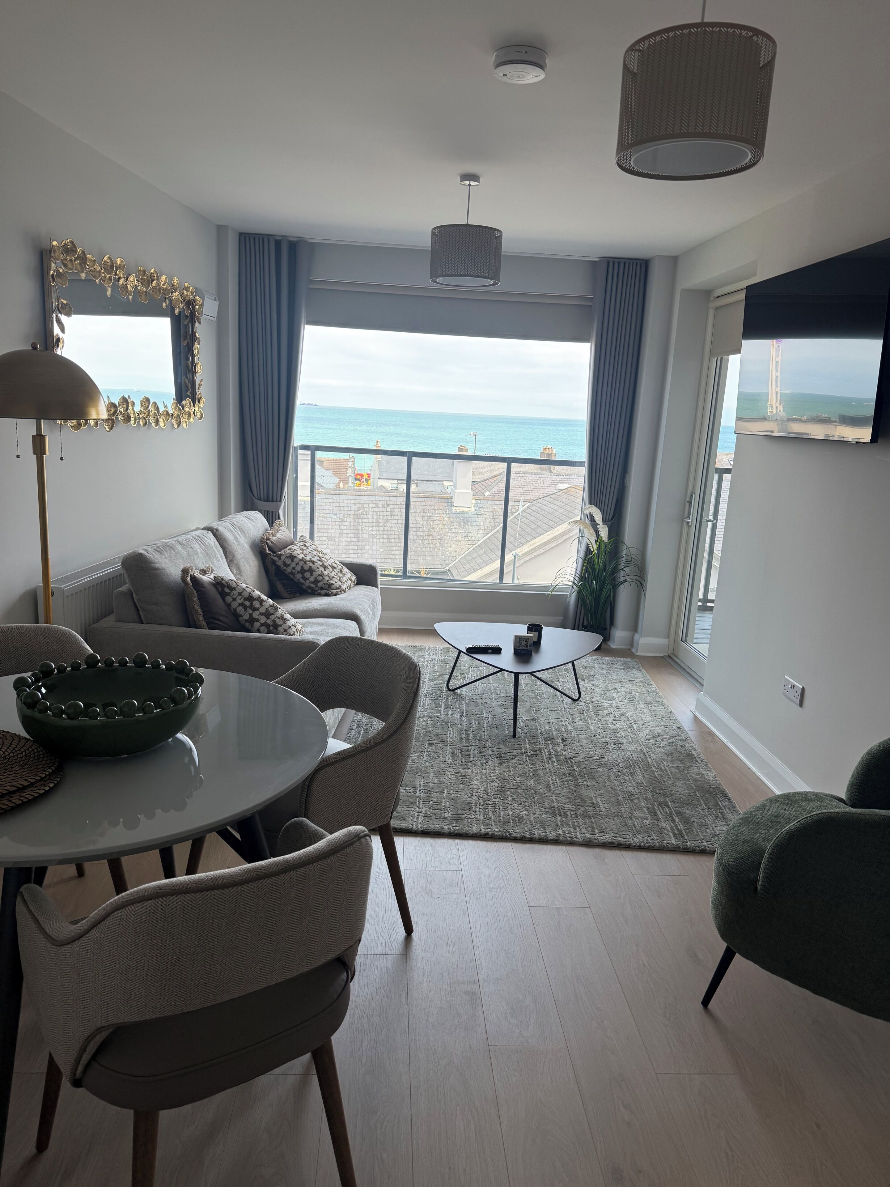 Ein modernes Wohnzimmer mit Meerblick, einer Essecke und einem Sofa mit Zierkissen.