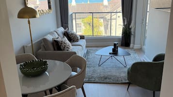 A modern living room with a sofa, dining table, chairs, a coffee table, and a view of the sea through large windows.