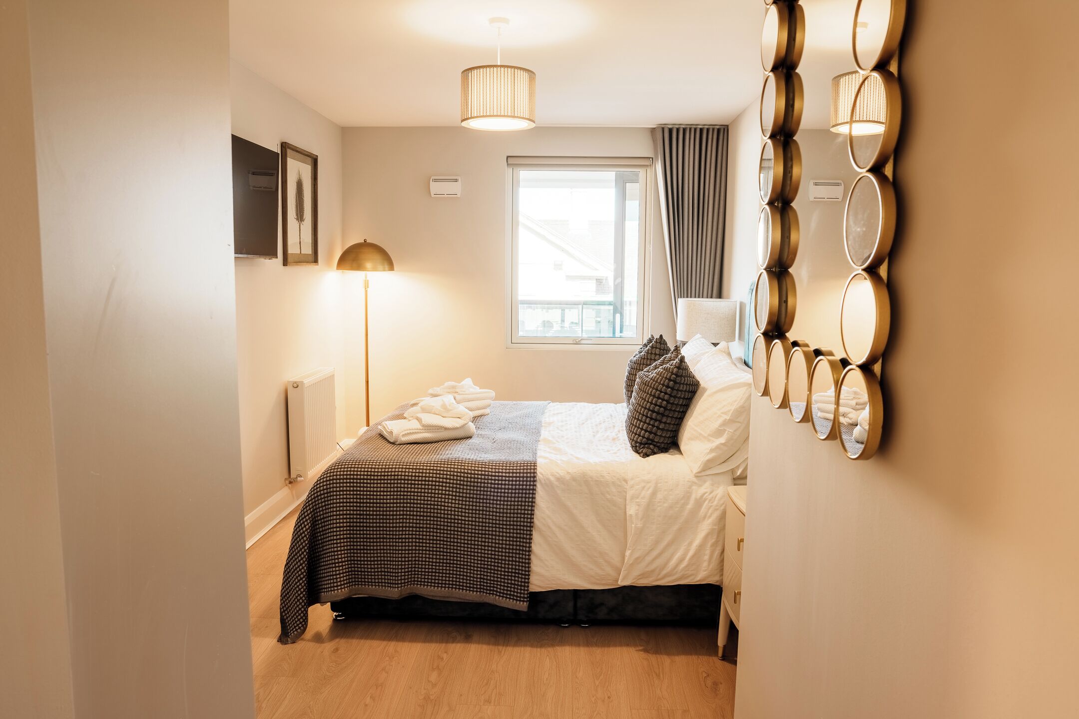 Une chambre d’hôtel comprenant un lit, une lampe sur pied, un radiateur, une fenêtre avec des rideaux et un miroir fixé au mur.