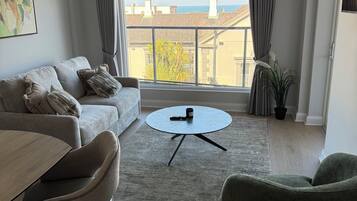 Uma sala de estar moderna com um sofá, cadeiras, uma mesa de centro e vista para o mar através de grandes janelas.
