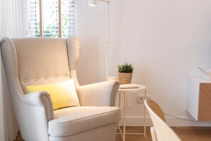 Een moderne woonkamer met een lichtgrijze fauteuil, een bijzettafeltje met een plant en een vloerlamp.