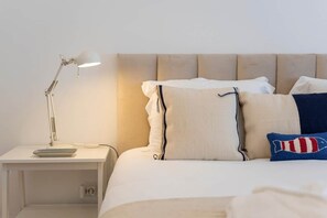 Een net opgemaakt bed met een hoofdeinde, een bedlampje en een klein tafeltje met een afstandsbediening.