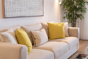 Ein beiges Sofa mit gelben Kissen, ein großes abstraktes Gemälde an der Wand und eine Bambuspflanze in der Ecke.