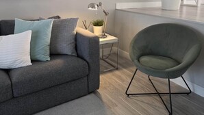 Ett modernt vardagsrum med en grå soffa, en grön fåtölj, ett litet sidobord med en lampa och en krukväxt.