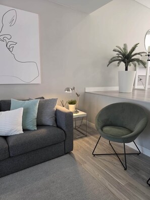 Ein modernes Wohnzimmer mit einem grauen Sofa, einem grünen Sessel, einem kleinen Beistelltisch mit einer Lampe und einem Blumentopf.