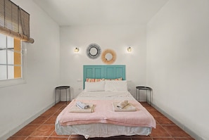Quarto com cama, duas mesas de cabeceira, janela com persianas e luminárias fixadas na parede.