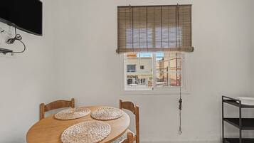 Un comedor con una mesa y sillas de madera, una ventana con persianas y un televisor montado en la pared.
