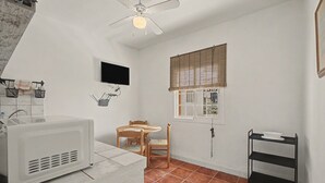 Une cuisine compacte équipée d’un four à micro-ondes, d’une table en bois avec des chaises, d’une fenêtre avec des stores et d’un ventilateur de plafond.