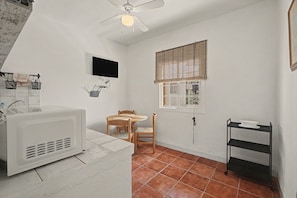 Una cocina compacta con microondas, una mesa de madera con sillas, una ventana con persianas y un ventilador de techo.