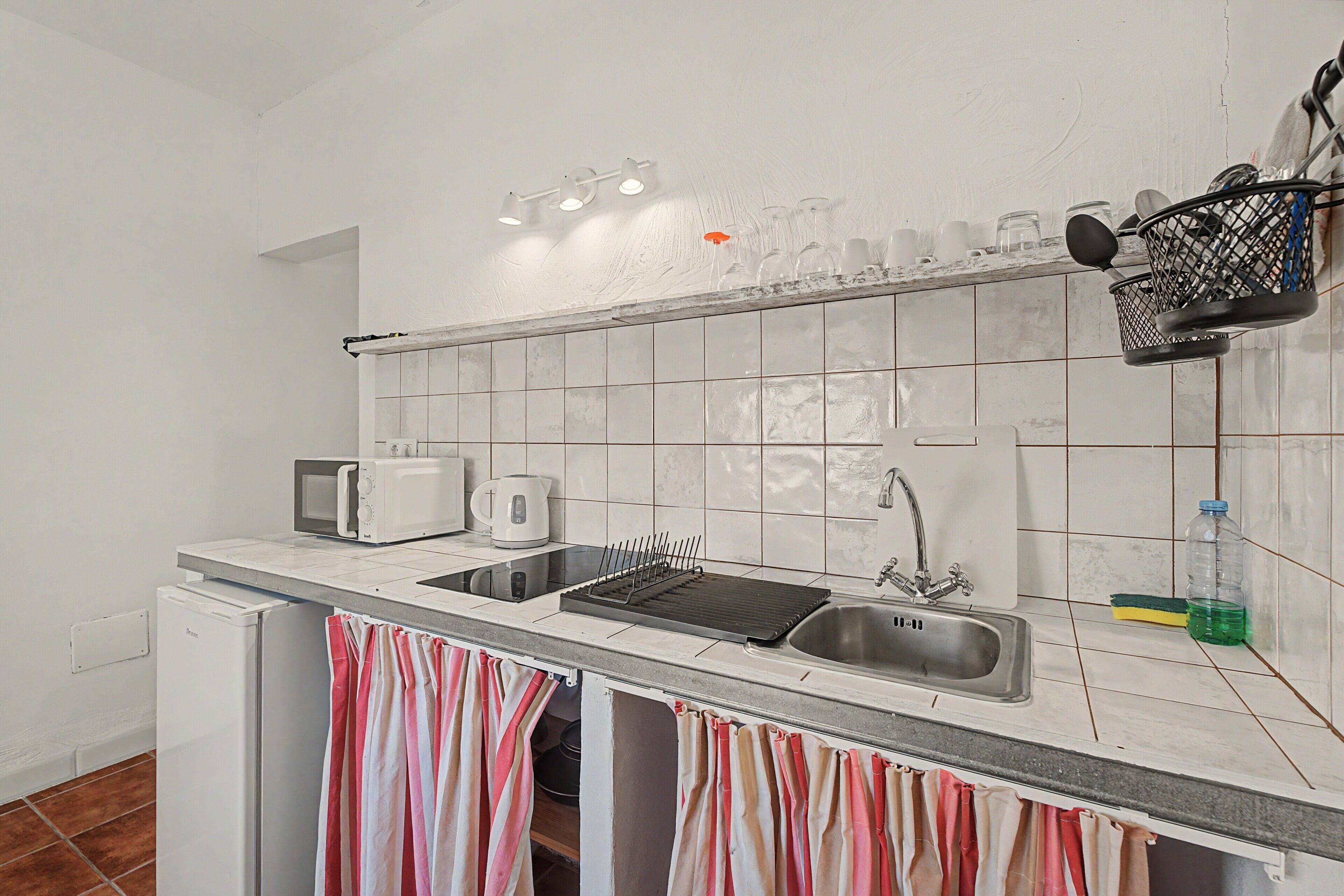 Una cocina equipada con microondas, hervidor, tostadora y pileta con escurridor.