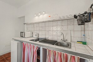 A kitchen with a microwave, kettle, toaster, and a sink with a drying rack.