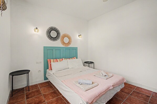 A bedroom with a bed, two bedside tables, a wall-mounted light fixture, and a decorative mirror.