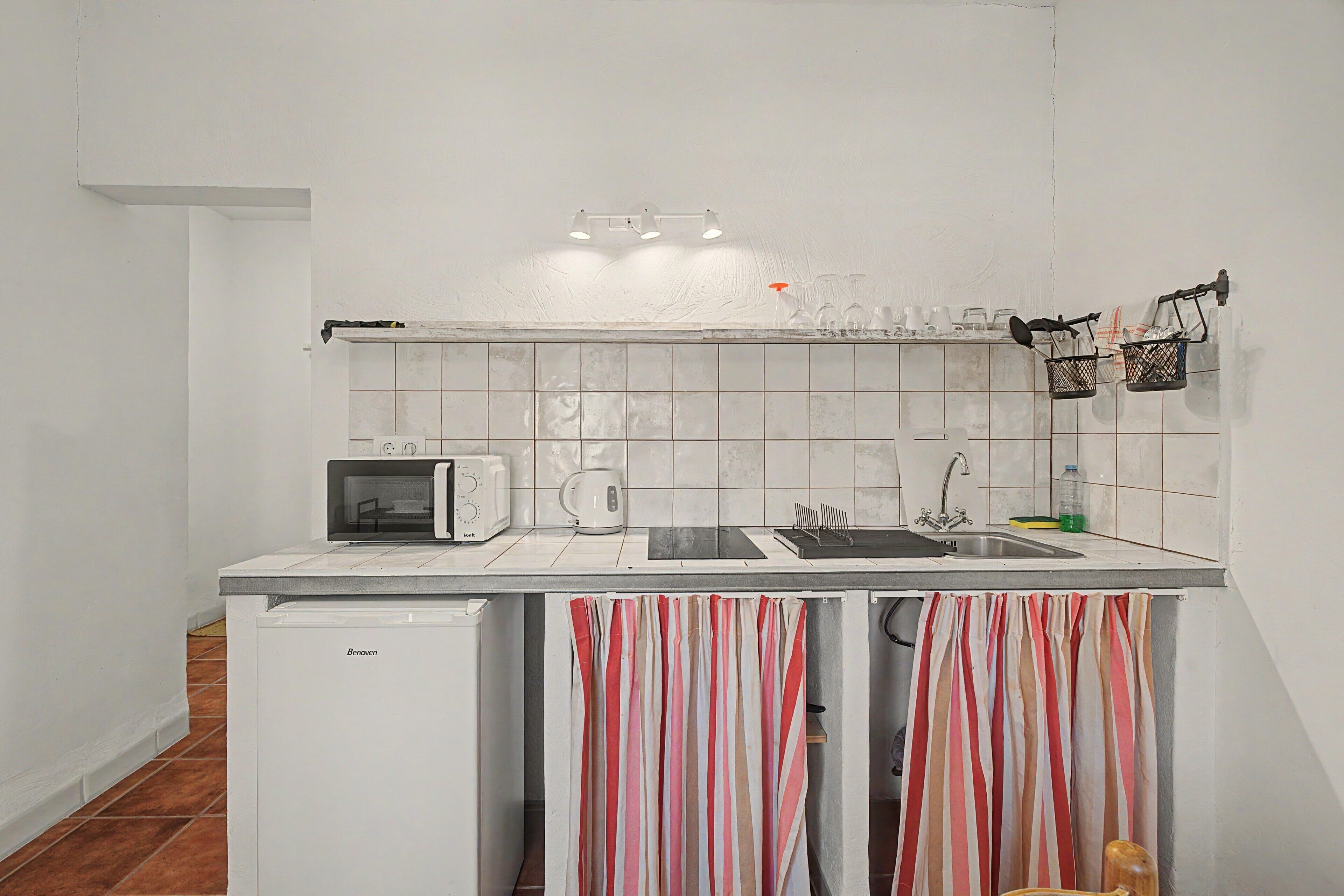 Una cocina compacta con microondas, hervidor y lavamanos.