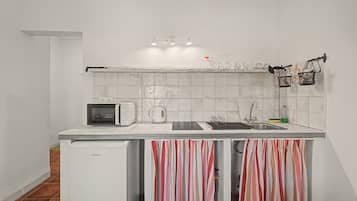 Una cocina compacta con microondas, hervidor y lavamanos.