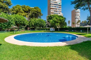 Une piscine entourée de pelouse et d’arbres, avec de grands immeubles en arrière-plan.