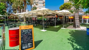 An outdoor café with tables and umbrellas, surrounded by greenery and buildings. - Cubo's Playamar Beach Apartment / communal pool / terrace / air conditioning / free Wi-Fi (Torremolinos)