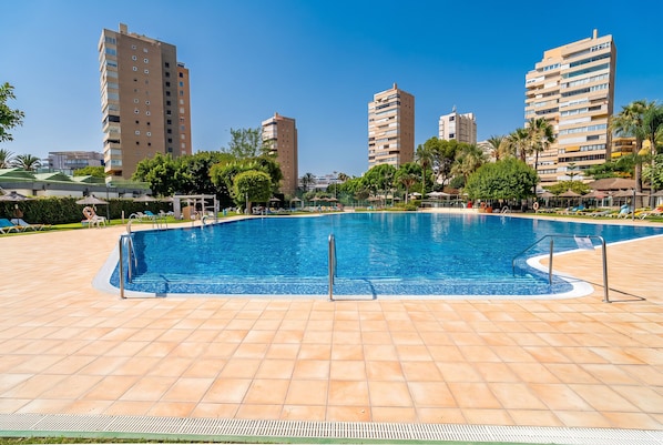 A swimming pool with a tiled deck, surrounded by palm trees and buildings. - Cubo's Playamar Beach Apartment / communal pool / terrace / air conditioning / free Wi-Fi (Torremolinos)