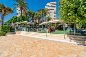 A courtyard with outdoor seating, palm trees, and a building in the background. - Cubo's Playamar Beach Apartment / communal pool / terrace / air conditioning / free Wi-Fi (Torremolinos)