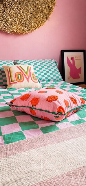 A bed with a checkered bedspread, a pillow with a floral pattern, and a pillow with the word 'LOVE' on it.