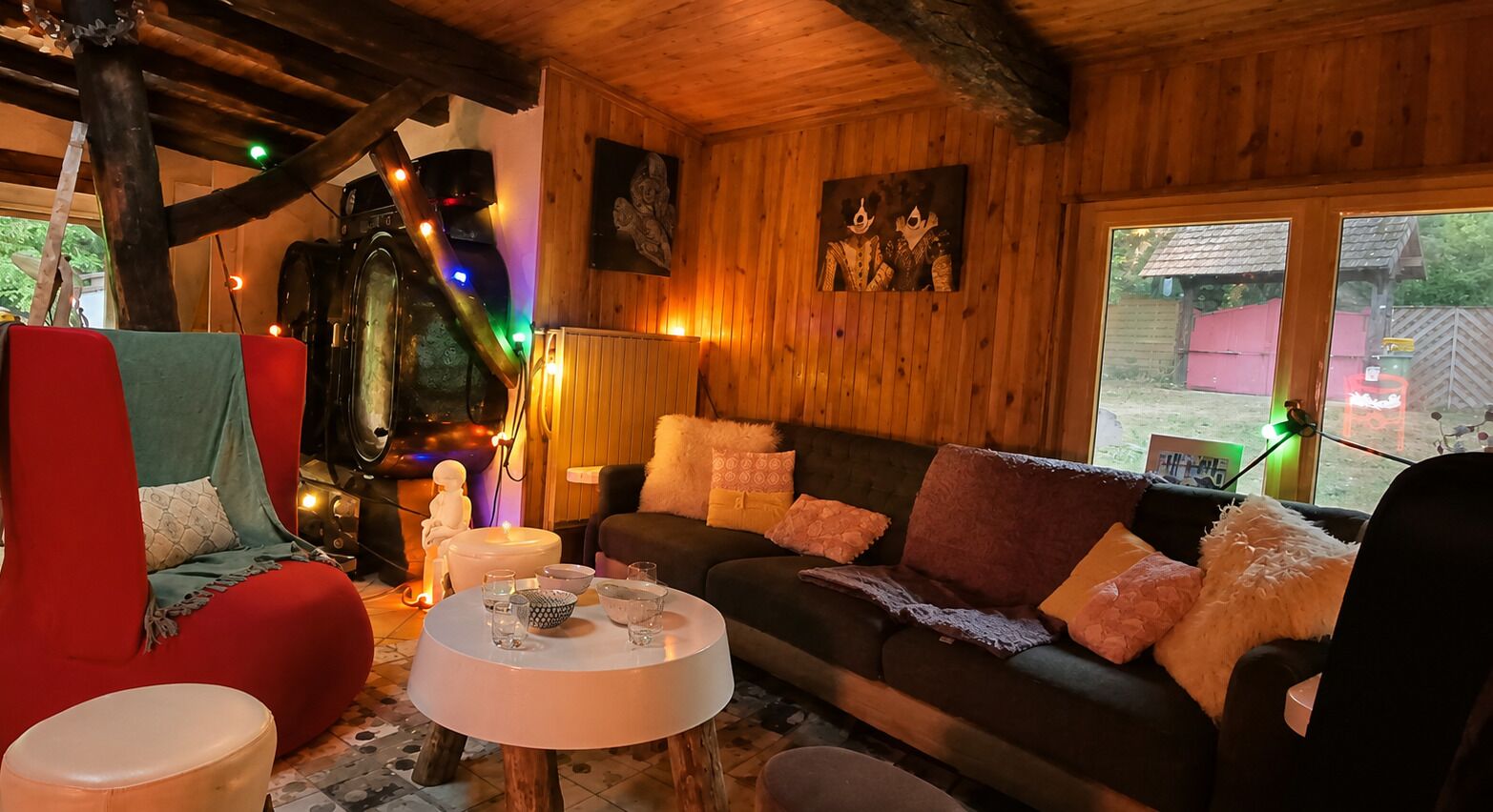 Ein gemütliches Zimmer mit Holzvertäfelung, einer Couch, einem roten Sessel und einem kleinen runden Tisch mit Gläsern und einer Schale.