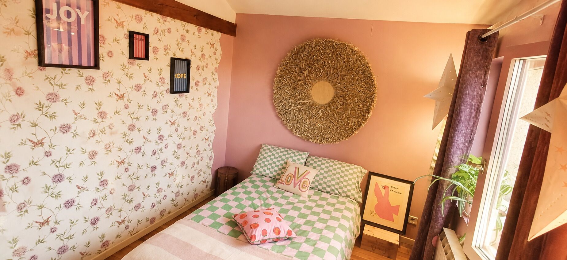 A bedroom with floral wallpaper, a checkered bedspread, and a circular wall decoration.