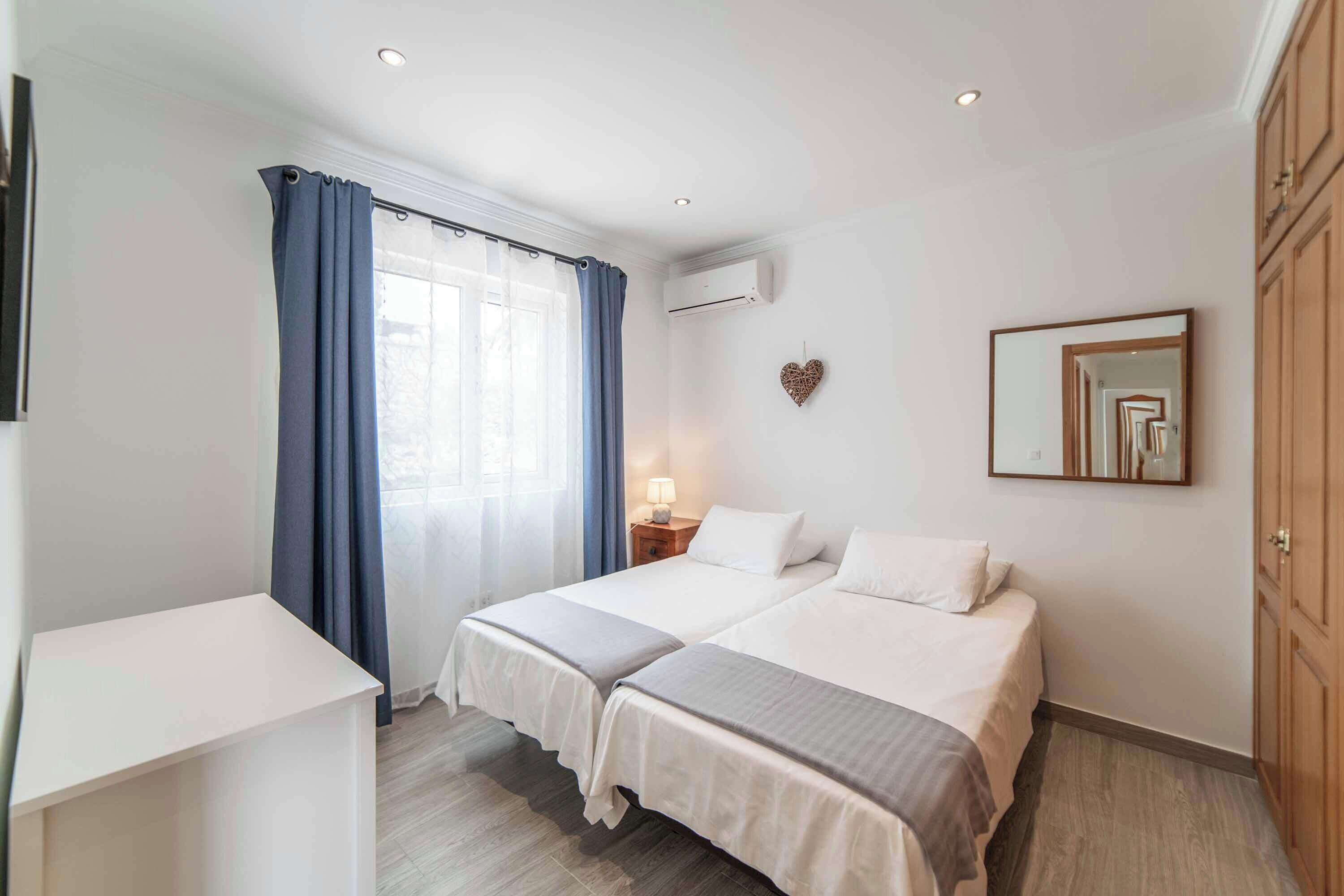 Ein Hotelzimmer mit zwei Betten, einem Schreibtisch, einer Nachttischlampe, einer Klimaanlage und einem wandmontierten Spiegel.