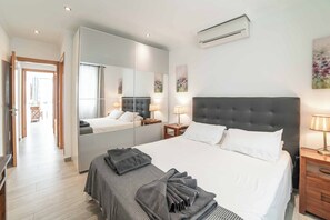 Ein Hotelzimmer mit einem großen Bett, einem Spiegel, einem Nachttisch mit Lampe und einer Wand-Klimaanlage.