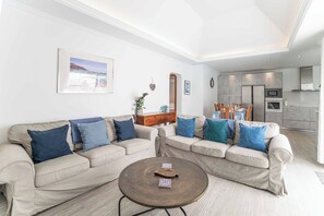 A living room with a beige sofa, a coffee table, and a dining area with wooden chairs. - Villa Botanica - Four Bedroom Villa, Sleeps 8 (Playa Blanca)