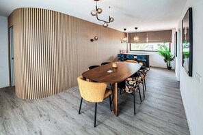 Ein moderner Essbereich mit einer Holzwand, einem runden Tisch und Stühlen mit floralem Bezug.