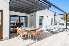 Um pátio moderno ao ar livre com mesa e cadeiras de jantar, uma área de estar coberta e vista para a cidade.