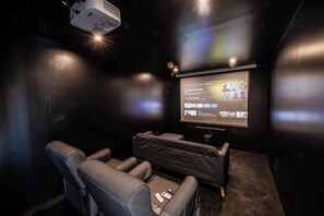 Ein dunkler Raum mit einer großen Leinwand, zwei Liegesesseln und einem Projektor.