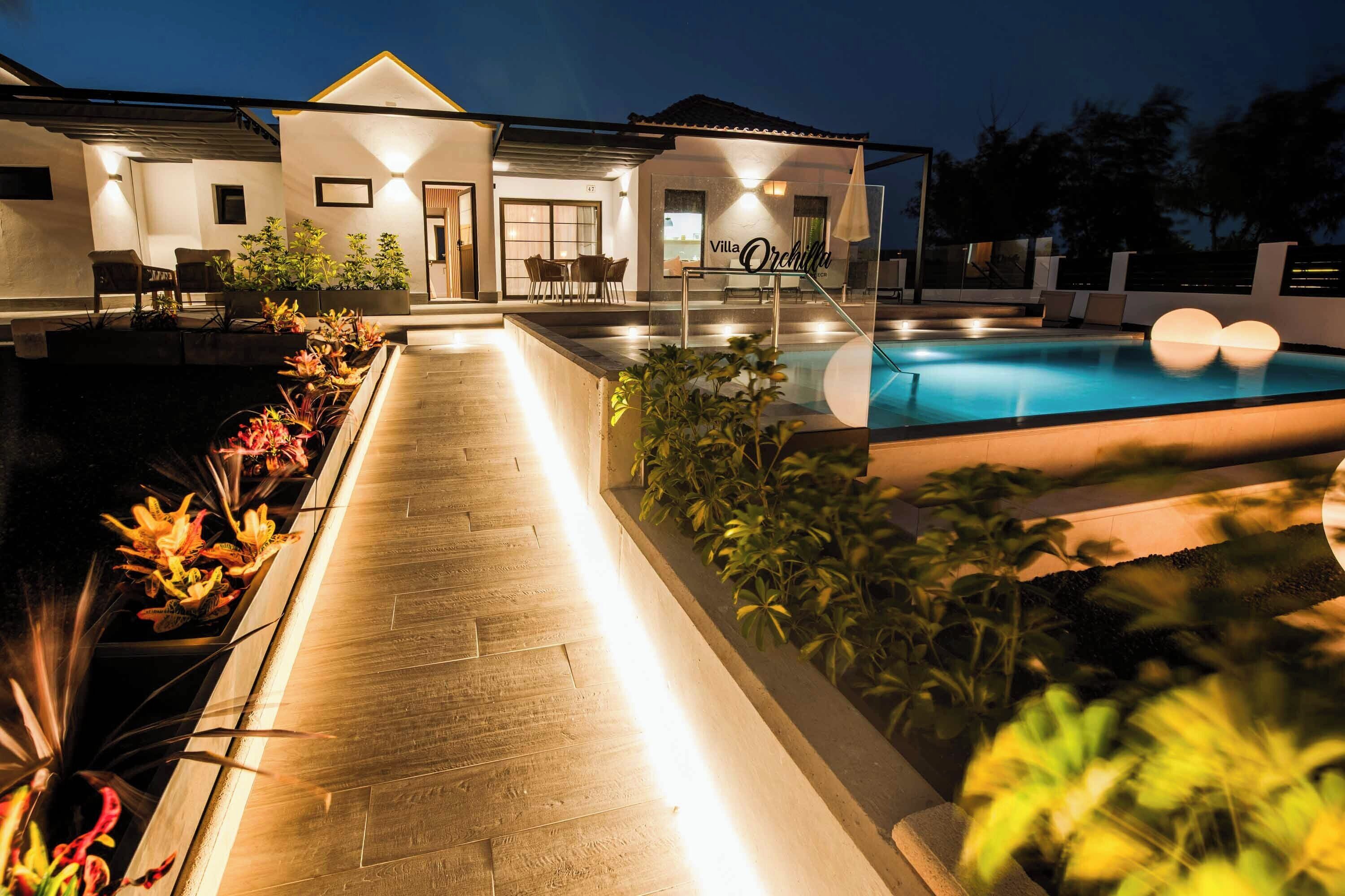 Una villa moderna con piscina, mobiliario exterior e iluminada senda.