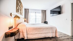 Ett hotellrum med en säng, sänglampor, en platt-TV och ett fönster med gardiner.