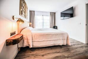 Ein Hotelzimmer mit Bett, Nachttischlampen, einem Flachbildfernseher und einem fenster mit Vorhängen.