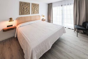 Une chambre d’hôtel avec un grand lit, une table de chevet, une lampe, une chaise et une fenêtre avec des rideaux.
